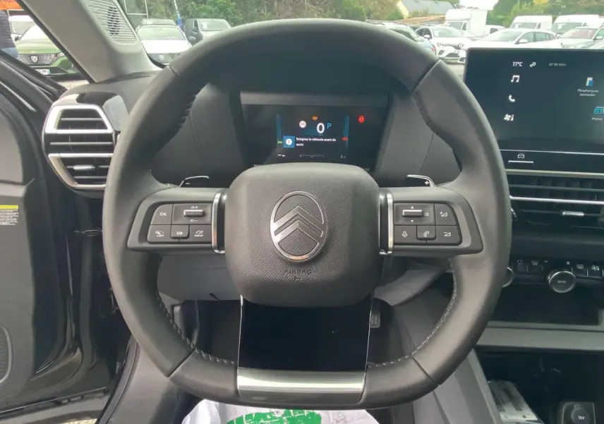 Vue centrée sur le volant noir du Citroën C4 hybride 2025, avec tableau de bord numérique et écran tactile visible.