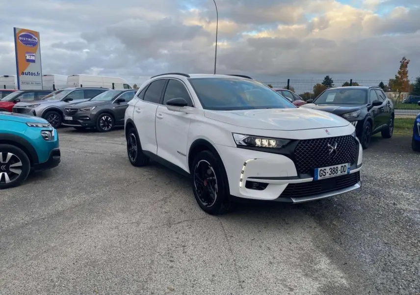 DS7 Crossback blanc en 3/4 avant droit avec calandre noire et jantes noires sur parking extérieur.