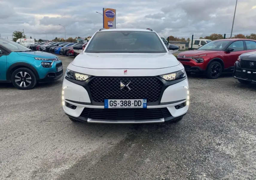Vue frontale d'un DS7 Crossback blanc 2022 avec calandre noire et feux LED allumés sur un parking.