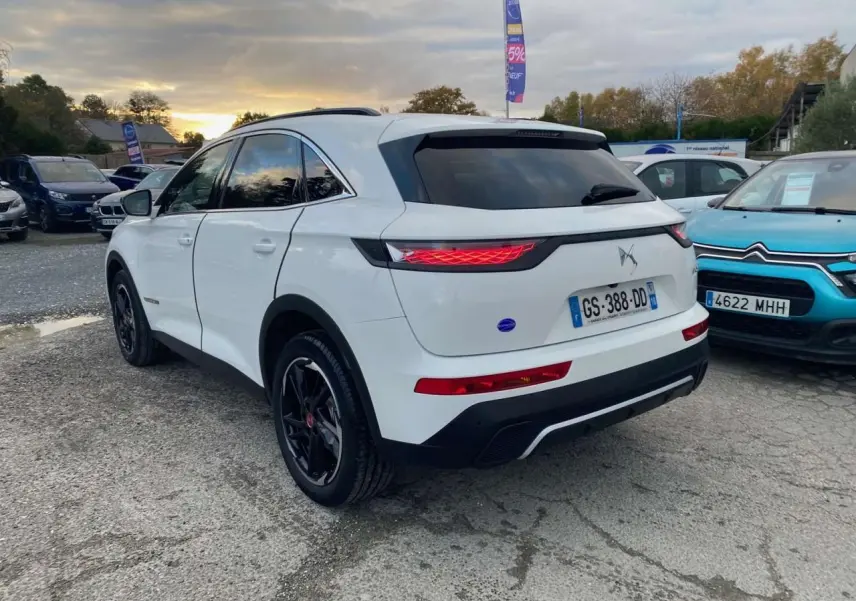 Vue 3/4 arrière droite d'un DS7 Crossback blanc 2022 avec jantes noires et feux arrière allumés.