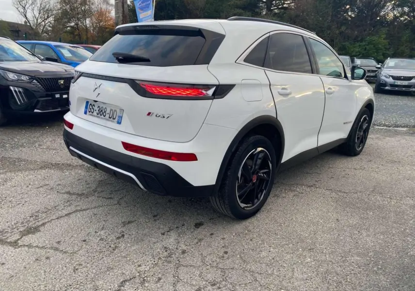 Vue 3/4 arrière droite du SUV blanc DS7 Crossback 2022 avec feux arrière allumés et jantes noires.