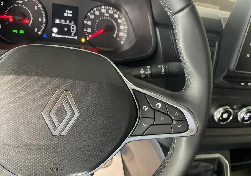 Vue rapprochée du volant noir du Renault Trafic Fourgon avec commandes intégrées et tableau de bord en arrière-plan.