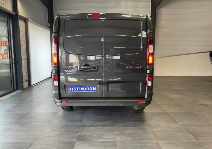 Vue arrière d’un Renault Trafic Fourgon gris comète avec feux allumés dans un showroom intérieur.