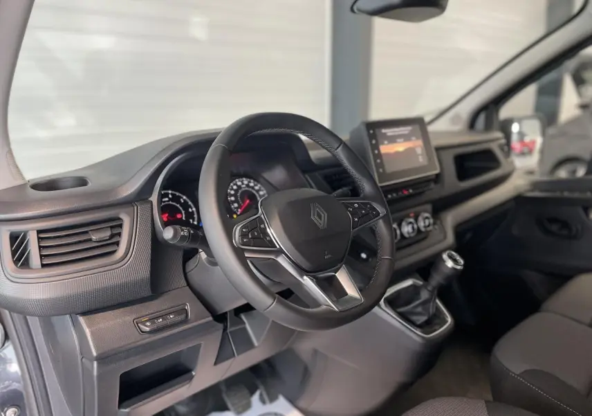 Vue intérieure côté conducteur du Renault Trafic Fourgon gris Comète, montrant le volant, tableau de bord et écran tactile central.