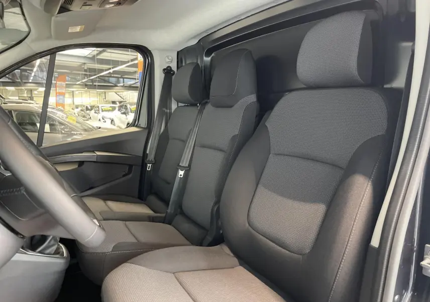Vue intérieure côté conducteur du Renault Trafic Fourgon gris Comète, montrant les sièges avant et la cloison tôlée arrière.