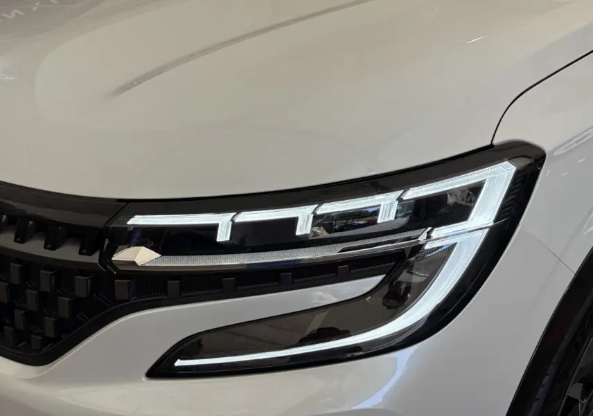 Gros plan sur le phare avant droit allumé du Renault Espace Esprit Alpine blanc, soulignant la signature lumineuse LED distinctive.