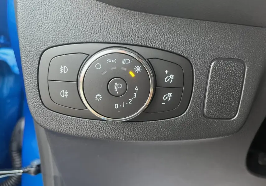 Gros plan sur le bouton de réglage des phares dans l'habitacle d'une Ford Puma bleu visible en arrière-plan.