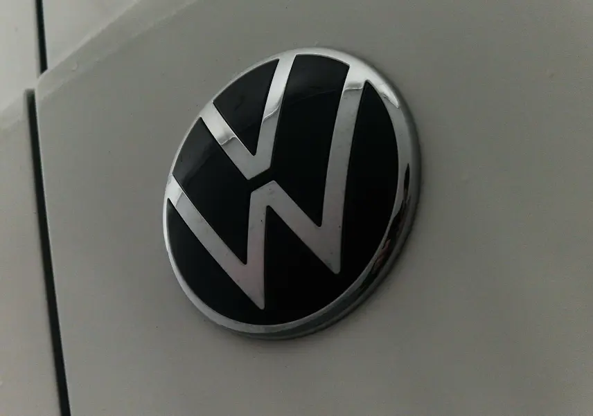 Gros plan sur le logo Volkswagen noir et chrome sur la carrosserie blanche du Caddy Maxi 4Motion.