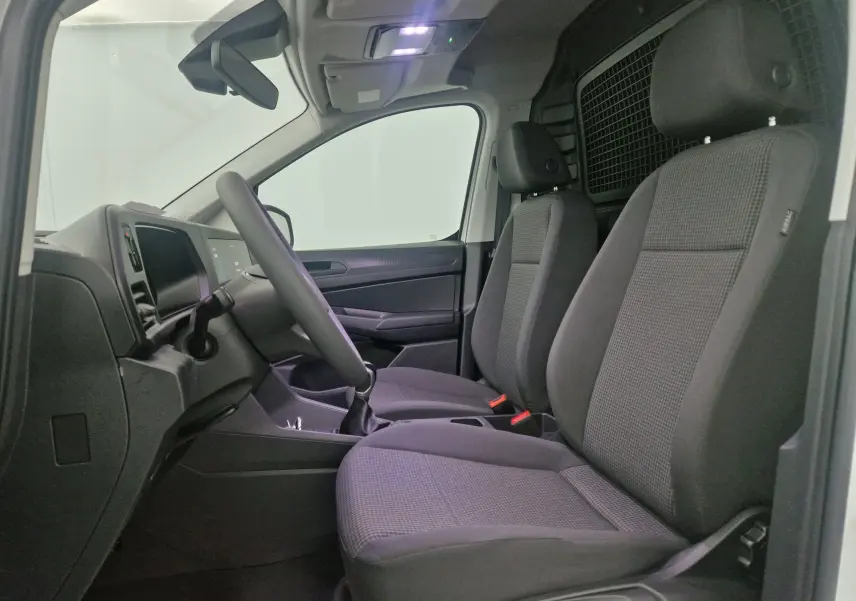 Vue intérieure côté conducteur du Volkswagen Caddy Maxi blanc 2025, sièges tissu gris et séparation métallique arrière.
