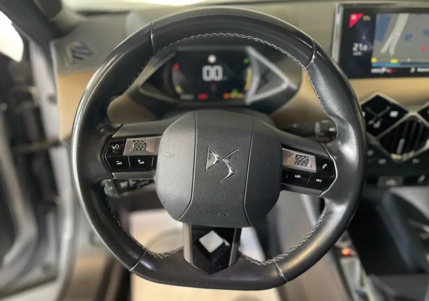 Vue rapprochée du volant en cuir noir du DS3 Crossback avec commandes intégrées et tableau de bord numérique en arrière-plan.