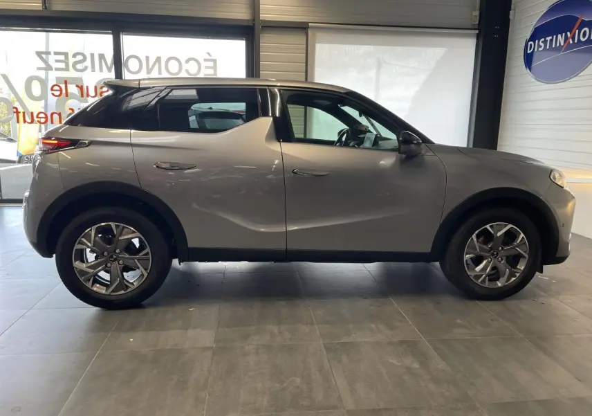 Profil côté gauche du DS3 Crossback gris Artense avec jantes alliage et toit noir en intérieur showroom.