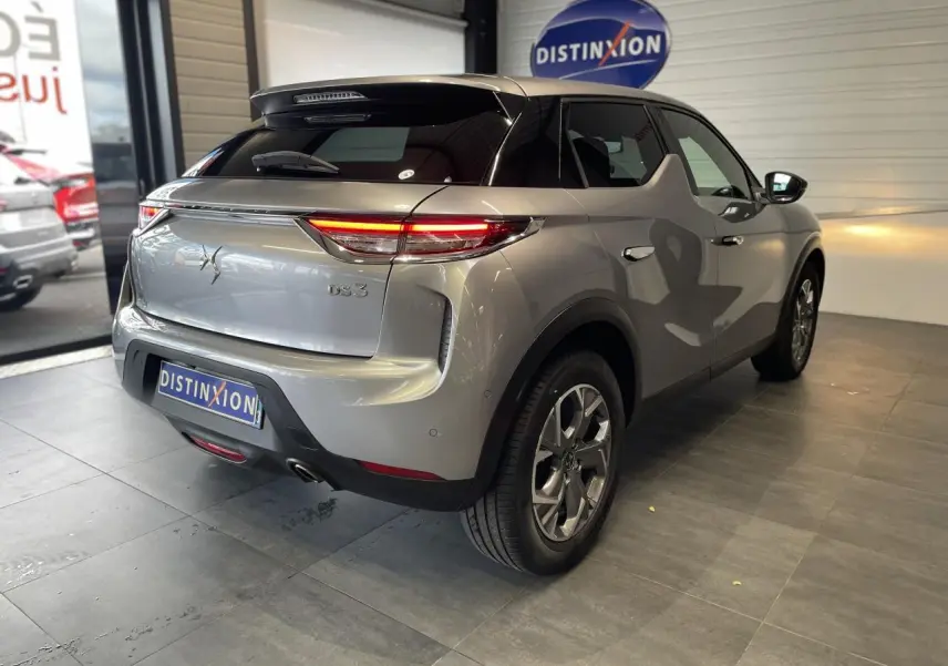 Vue 3/4 arrière droite d'un DS3 Crossback gris Artense avec toit noir et jantes alliage 17 pouces en showroom.
