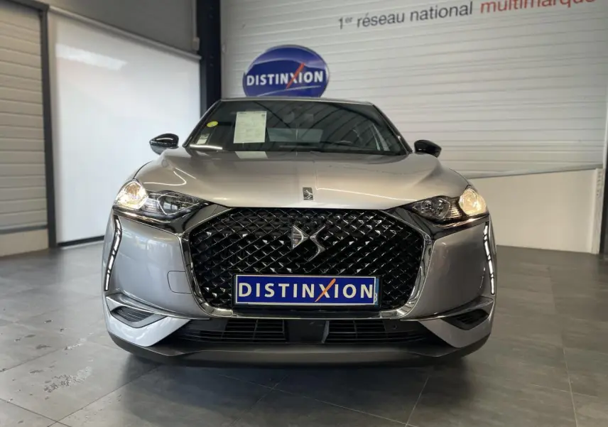 Vue de face du DS3 Crossback gris Artense, mettant en valeur sa calandre noire distinctive et ses phares allumés.