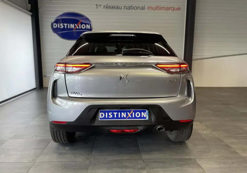 Vue arrière d'une DS3 Crossback gris Artense avec feux LED allumés et toit noir en showroom.