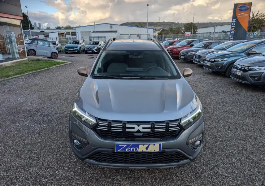 Vue avant d'un Dacia Jogger gris métallisé avec calandre noire et feux LED allumés sur un parking extérieur.