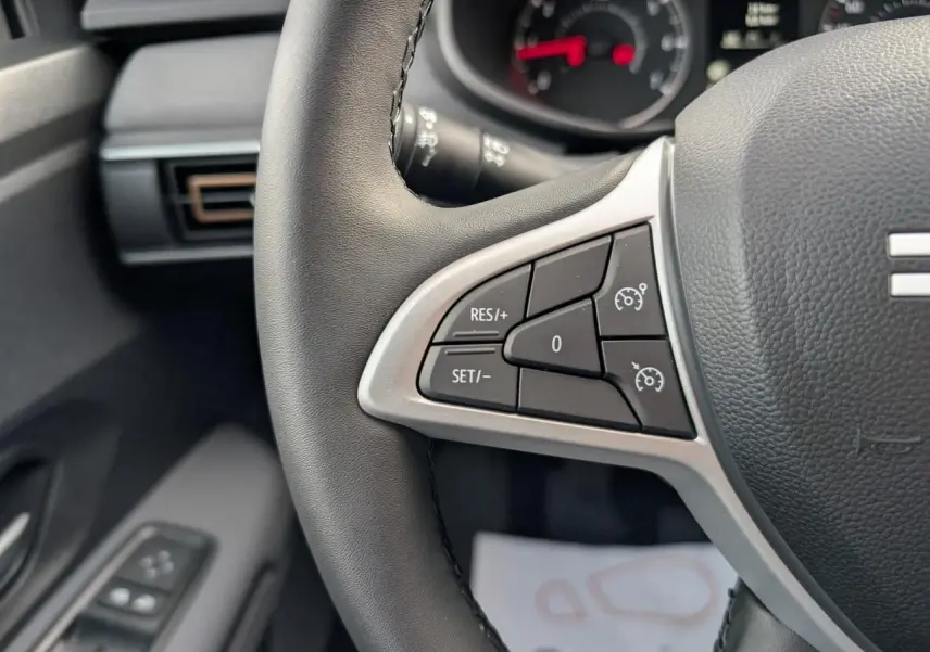 Gros plan sur les commandes du régulateur de vitesse au volant noir du Dacia Jogger, intérieur gris acier.