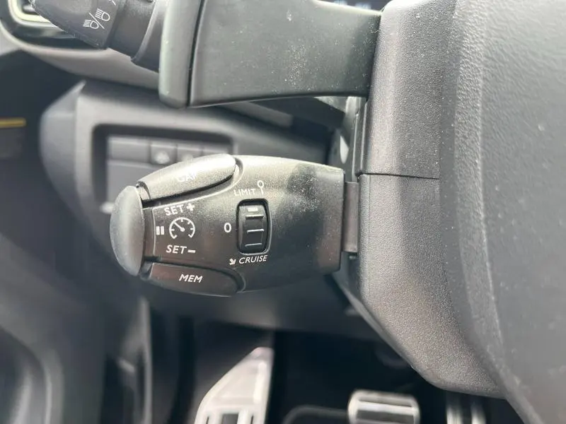 Gros plan sur la commande de régulateur de vitesse noire côté gauche du volant dans l'habitacle gris du Citroën C5 Aircross 2021.