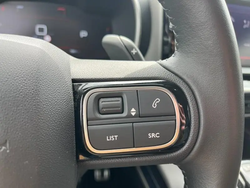 Gros plan sur les commandes du volant côté gauche du Citroën C5 Aircross gris acier, avec boutons LIST et SRC visibles.