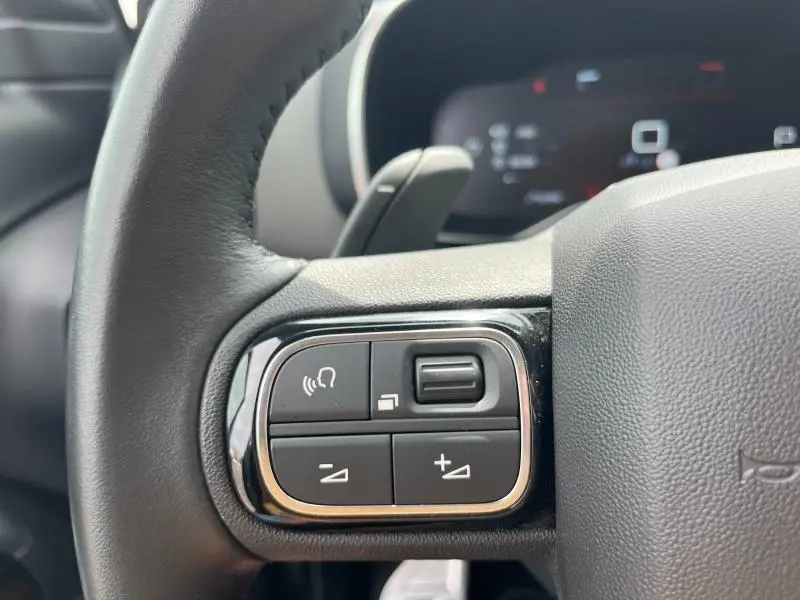 Gros plan sur les commandes du volant côté gauche du Citroën C5 Aircross gris acier, avec boutons multifonctions et finition noire.