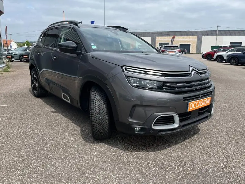 SUV Citroën C5 Aircross gris acier vu en 3/4 avant droit sur parking avec calandre noire brillante et jantes alu.