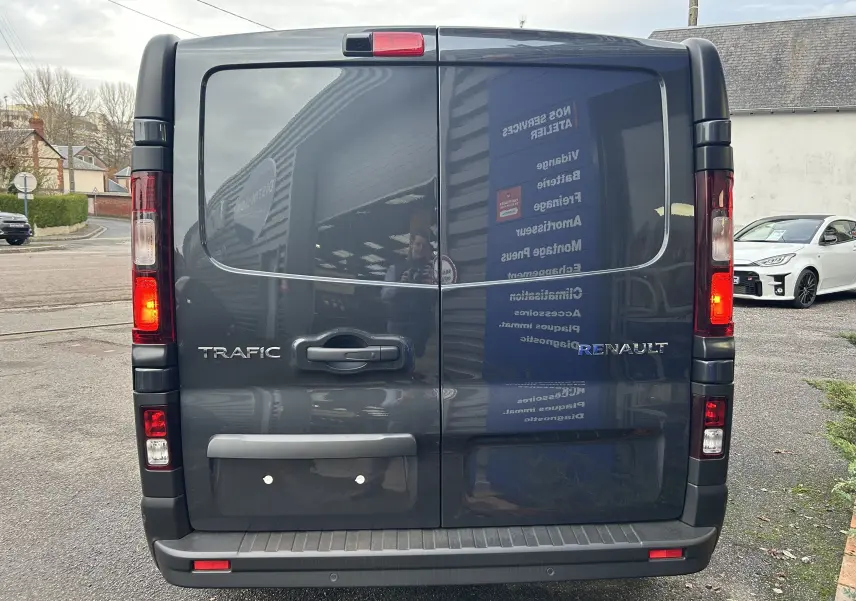 Vue arrière d’un Renault Trafic Fourgon gris Comète avec feux allumés et portes battantes fermées.