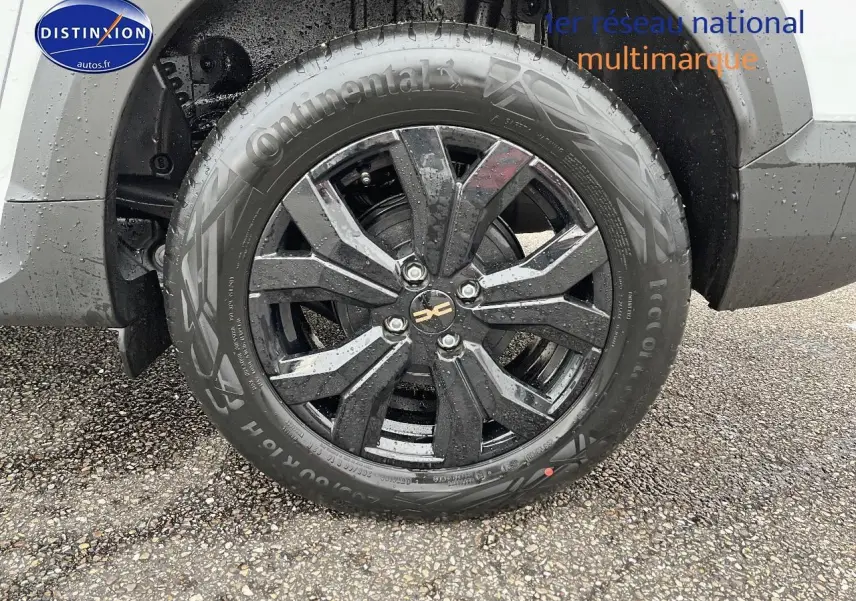 Gros plan sur la roue avant droite avec jante alu noire du Dacia Jogger blanc visible partiellement au-dessus.