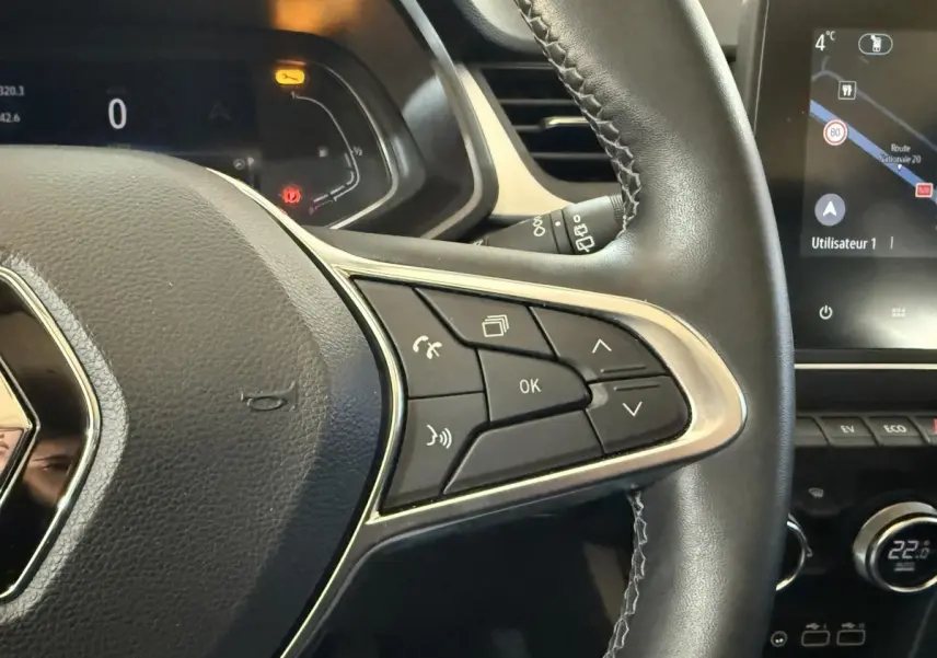 Gros plan sur le volant cuir synthétique noir du Renault Captur bleu 2024, avec commandes multifonctions et écran tactile visible.