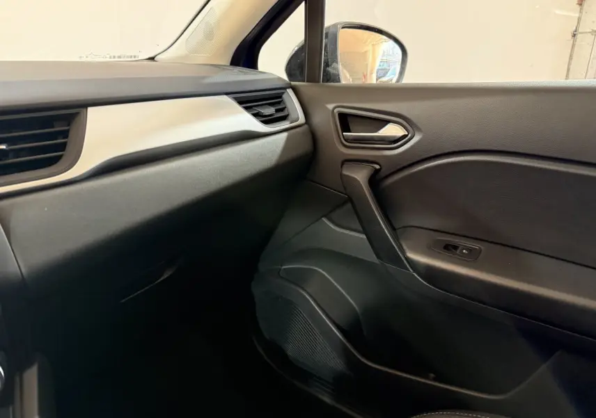 Vue intérieure côté passager du tableau de bord et de la porte noire du Renault Captur bleu, finition Evolution E-Tech 2024.