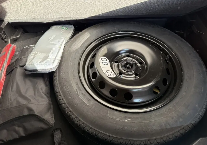 Gros plan sur la roue de secours noire dans le coffre du Renault Captur bleu 2024, avec trousse de secours à côté.