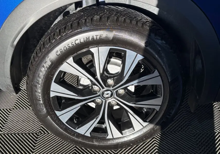 Gros plan sur la roue avant droite du Renault Captur bleu 2024 avec jante alliage bicolore et pneu Michelin CrossClimate.