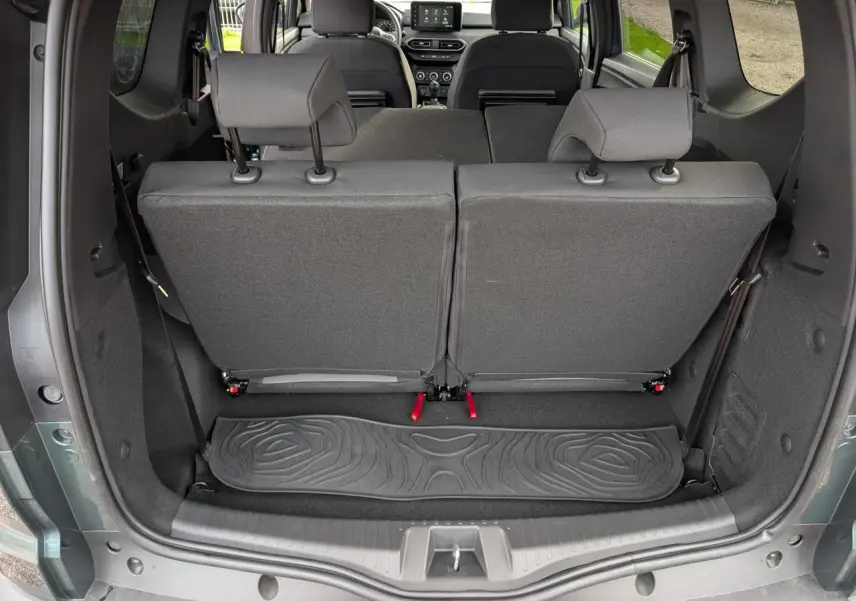 Vue arrière du coffre ouvert du Dacia Jogger vert métallisé, montrant les sièges de troisième rangée relevés et l'intérieur spacieux.