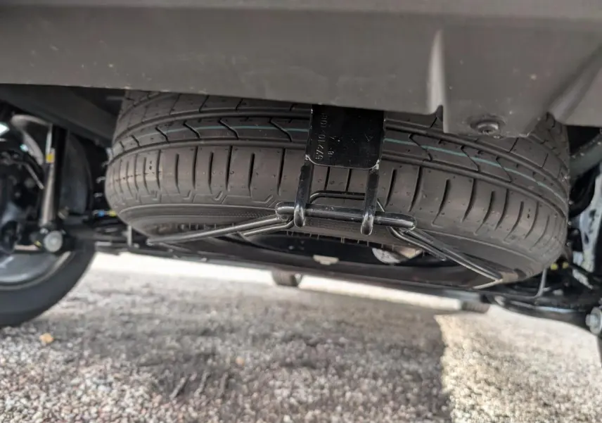 Gros plan sous le coffre montrant la roue de secours montée sous un Dacia Jogger vert métallisé.