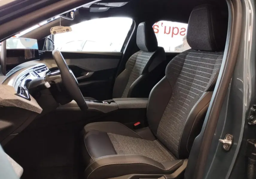 Vue intérieure côté conducteur du Peugeot 3008 2025 avec sièges tissu gris et cuir noir, planche de bord moderne et écran flottant.