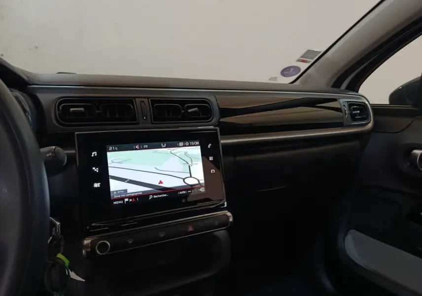 Vue intérieure côté passager du tableau de bord noir brillant avec écran tactile de navigation de la Citroën C3 blanche.