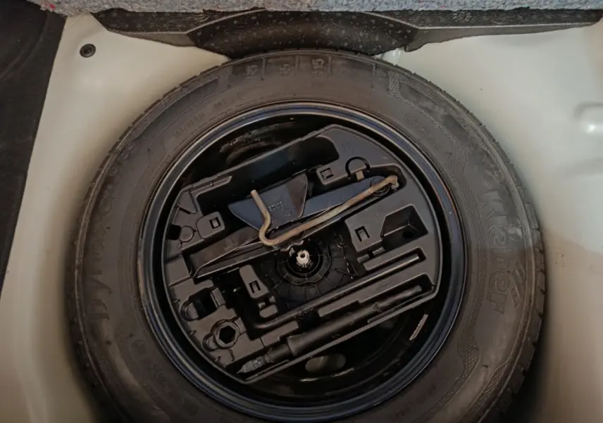 Vue plongeante sur la roue de secours noire et ses outils intégrés dans le coffre blanc d'une Citroën C3 2020.