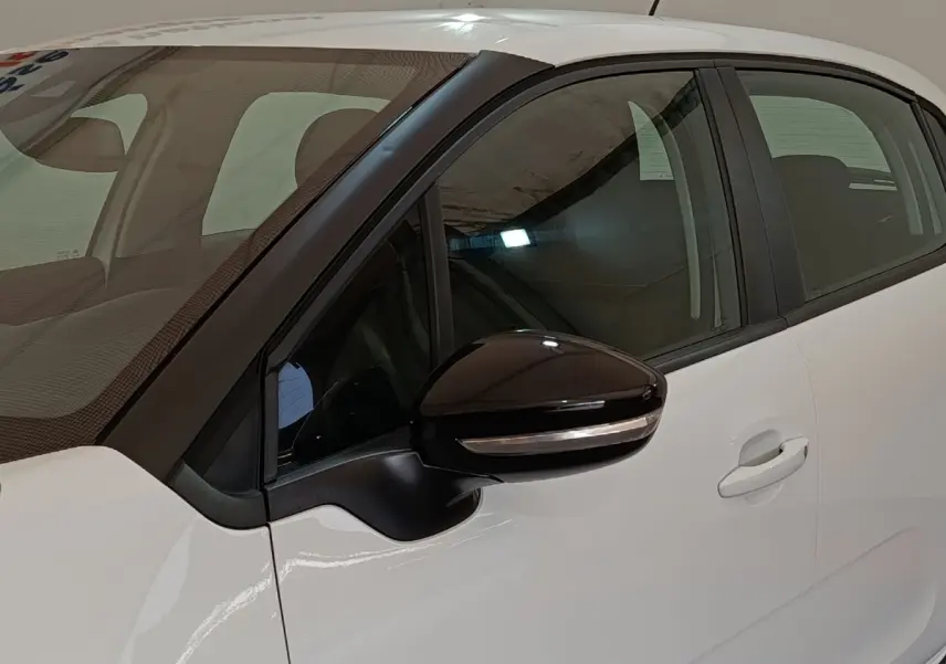 Vue rapprochée du côté gauche d'une Citroën C3 blanche avec rétroviseur noir et poignée de porte visible.