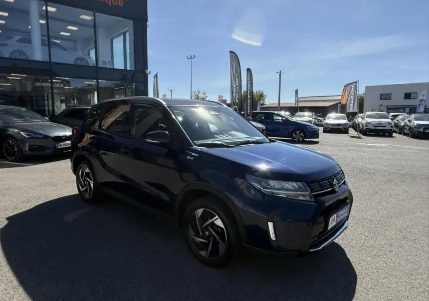 Suzuki Vitara 2025 bleu foncé métal en 3/4 avant droit, avec jantes alliage et badge Allgrip visible sur l'aile.