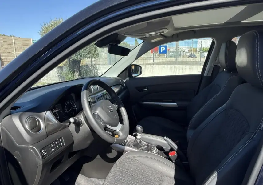 Vue intérieure côté conducteur du Suzuki Vitara 2025 bleu foncé, montrant le volant, la boîte manuelle et les sièges noirs.