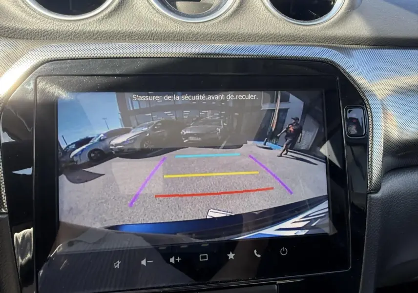 Vue de l'écran de recul du Suzuki Vitara bleu foncé métal 2025, avec lignes de guidage colorées et environnement arrière visible.