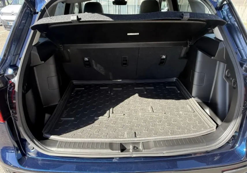Coffre ouvert vu de l'arrière d'un Suzuki Vitara 2025 bleu foncé métal, montrant le tapis de coffre et l'intérieur spacieux.