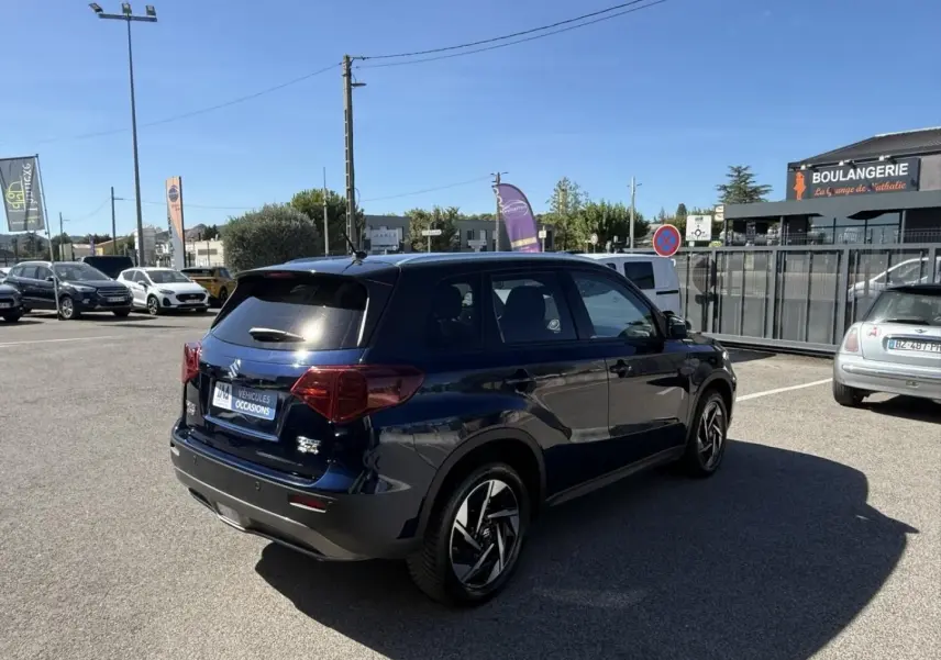 Suzuki Vitara 2025 bleu foncé métal, vue 3/4 arrière droit, jantes alliage distinctives et vitres teintées.