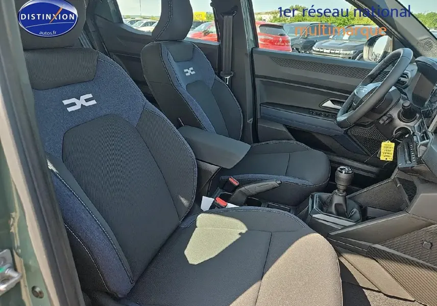 Intérieur du Dacia Duster 2025 vert kaki, vue côté gauche sur sièges tissu noir et bleu avec accoudoir central.