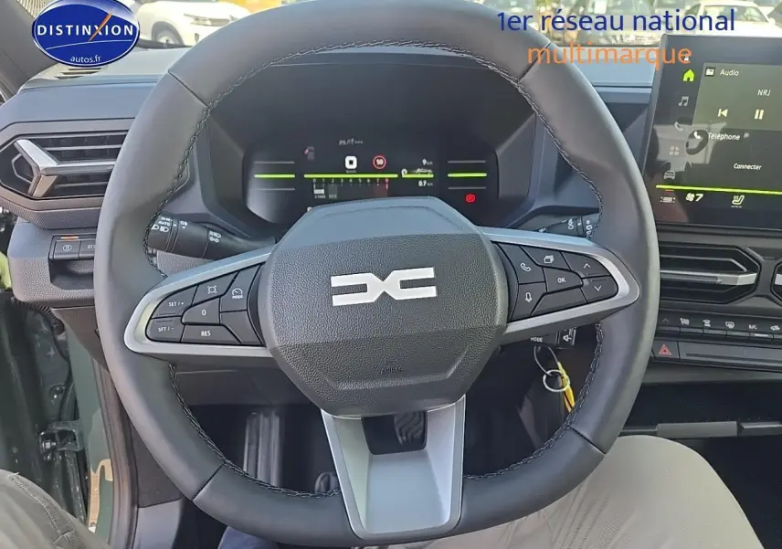Vue intérieure centrée sur le volant multifonction noir du Dacia Duster vert kaki 2025 avec tableau de bord digital et écran tactile.