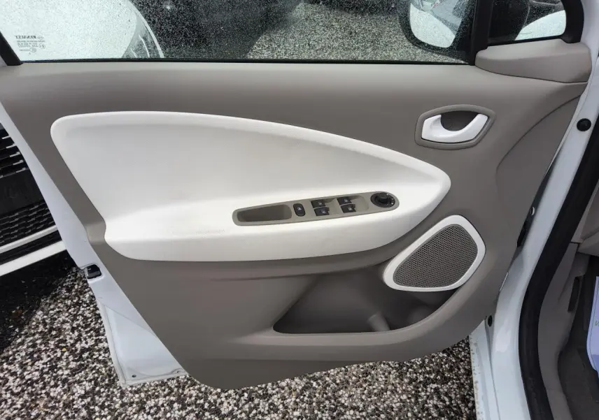 Porte avant gauche ouverte d'une Renault ZOE blanche, montrant le panneau intérieur beige et blanc avec commandes électriques.