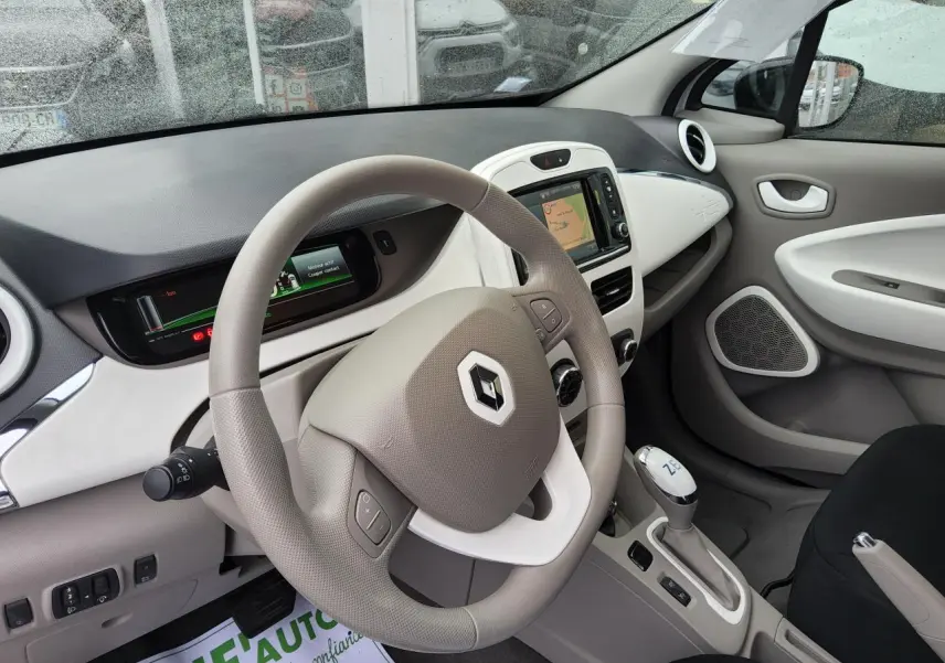 Intérieur de Renault ZOE blanc 2016 vu côté conducteur, volant beige avec logo Renault et console centrale moderne.