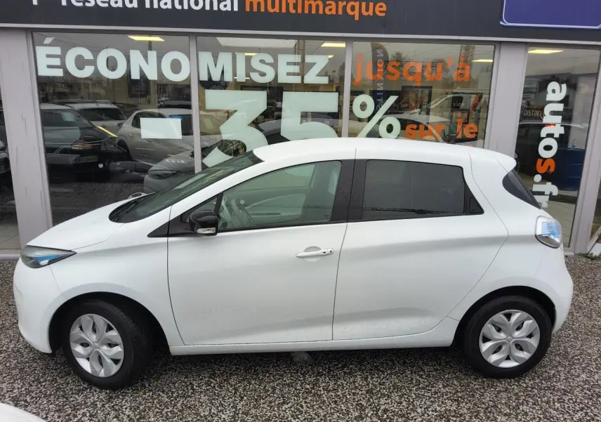 Profil côté gauche d'une Renault ZOE blanche Z.E. R240 Life, compacte avec vitres arrière surteintées et enjoliveurs 15 pouces.