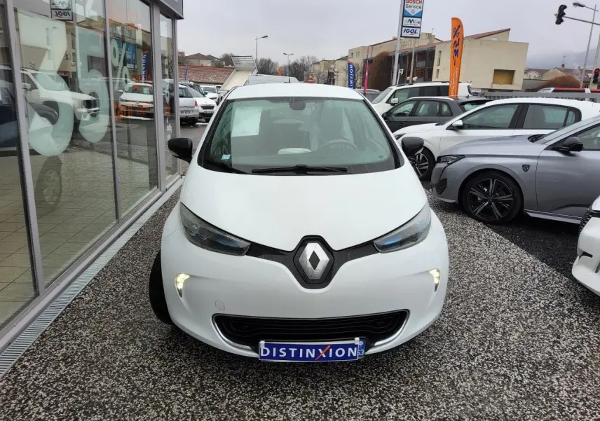 Vue avant d'une Renault ZOE blanche 2016 avec feux diurnes LED allumés sur un parking extérieur.