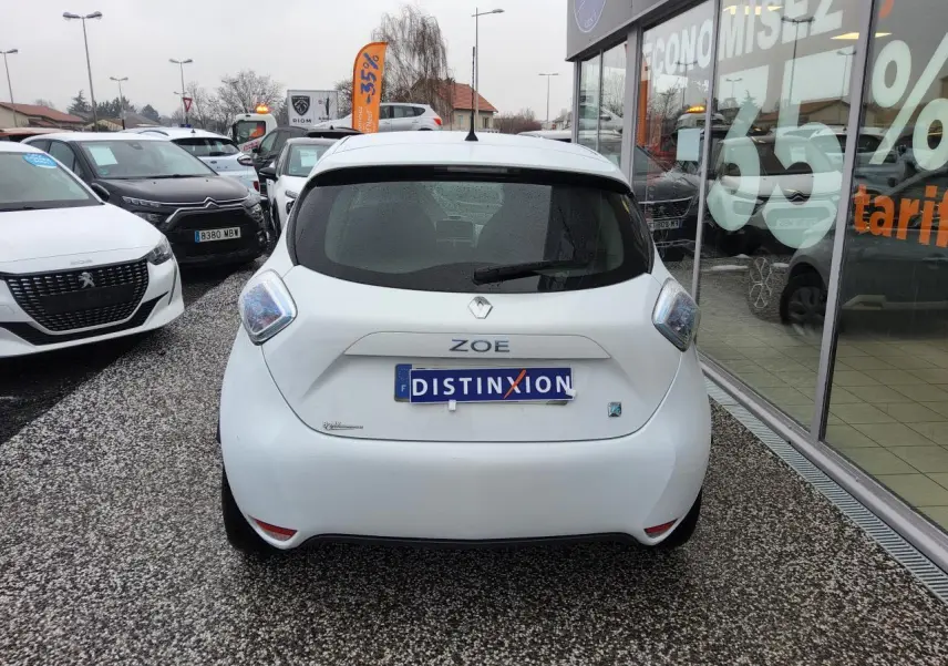 Vue arrière d'une Renault ZOE blanche 2016 avec badges ZOE et Z.E. sur un parking de concession.
