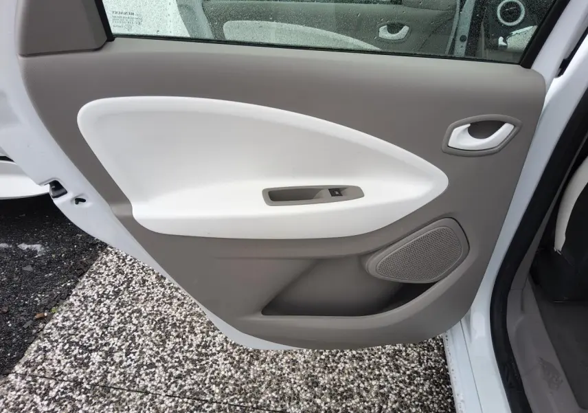 Porte arrière gauche ouverte de la Renault ZOE blanche, montrant le panneau intérieur beige et blanc avec commande de vitre.