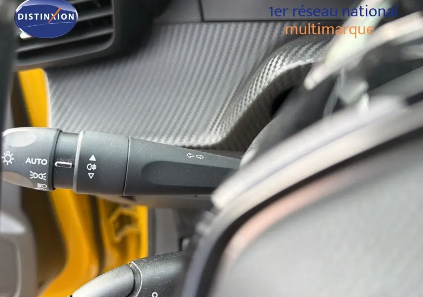 Gros plan sur la commande des feux et clignotants côté gauche du volant d'une Peugeot 208 électrique jaune Faro métal avec toit noir.
